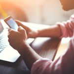 man using phone with laptop